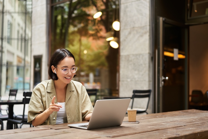 Ung kvinna arbetar med laptop utomhus på café.